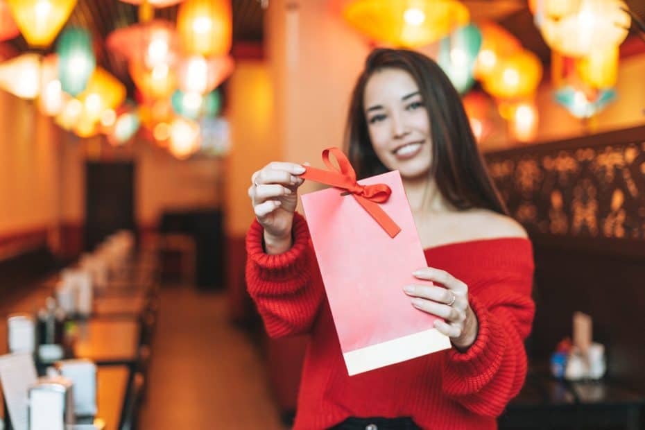 Beautiful young asian woman in red clothes with red gift bag in restaurant celebrating Christmas